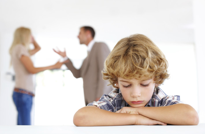 A sad young boy with his parents fighting in the background