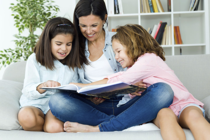 Portrait of beautiful mother with her daughters reading a book at home.