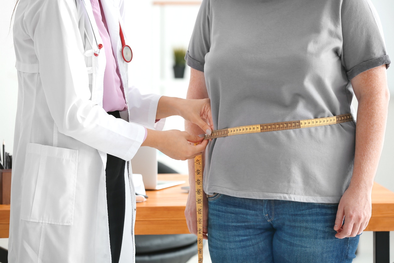 Young female doctor measuring waist of overweight woman with centimeter in clinic