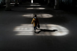 Lights hitting the floor from the window inside the building and a boy walking in the light Lights hitting the floor from the window inside the building and a boy walking in the light