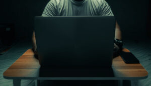 A man in a white shirt sits on a laptop in a dark room. with light shining down. internet concept addiction.topview. A man in a white shirt sits on a laptop in a dark room. with light shining down. internet concept addiction.topview.